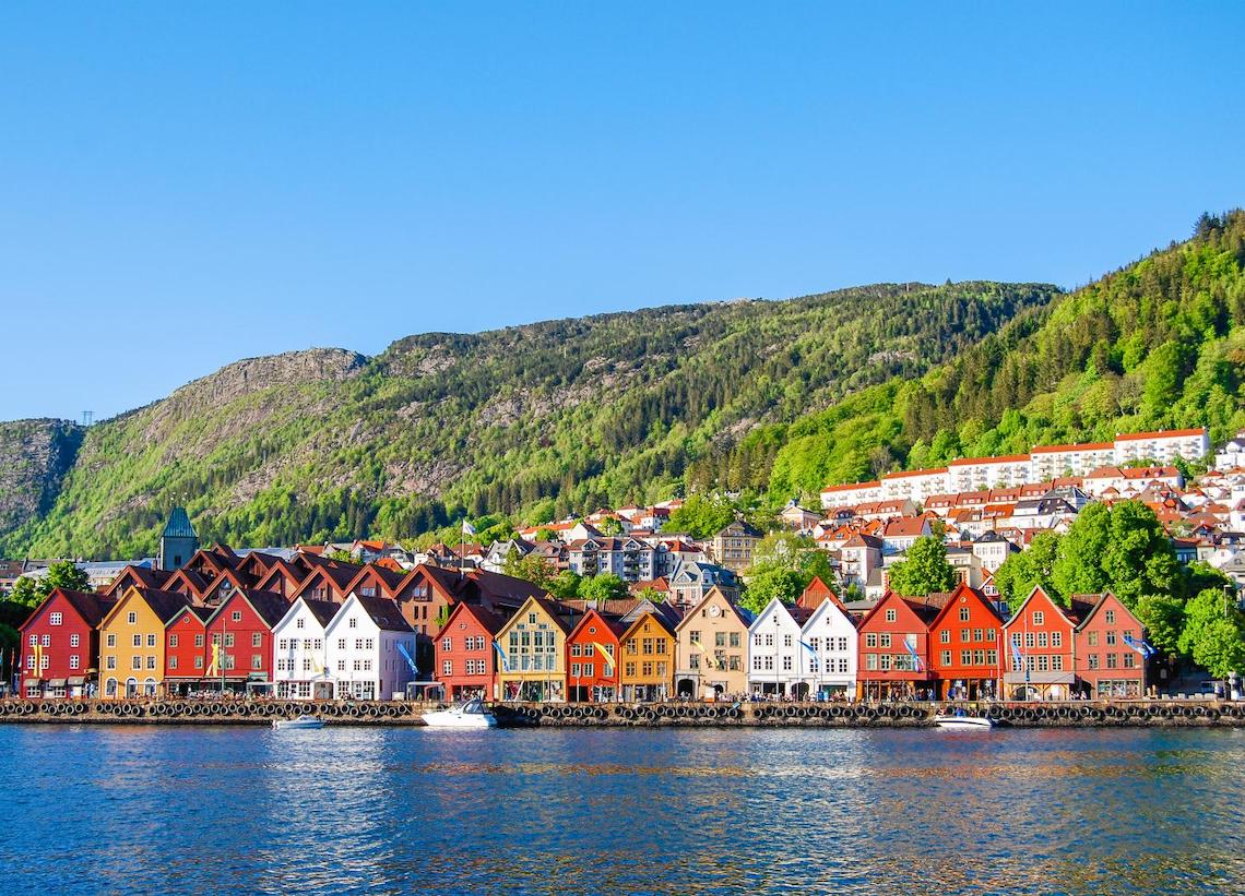 Colorful houses line Bergen Norway waterfront with mountains in background.